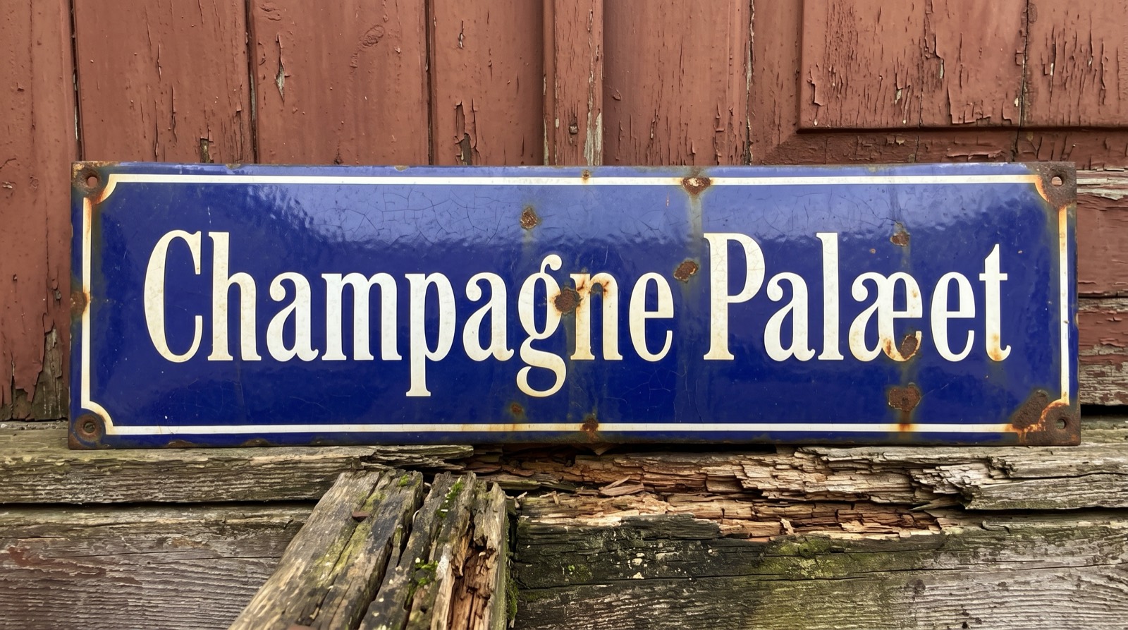 Vintage emaljeskilt med teksten Champagne Palæet på en rustik trævæg